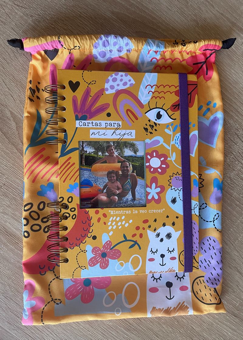 Cuaderno Cartas para mi hija: agenda argollada de tapa mostaza con ilustraciones de flores, gatos y arcoíris, ventana para la foto, elástico morado y su bolsa de tela a juego.