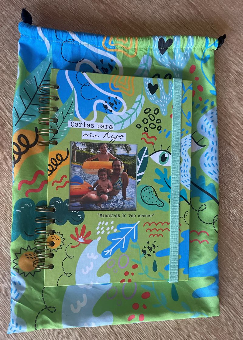 Cuaderno Cartas para mi hijo: agenda argollada de tapa verde con ilustraciones de hojas, gatos y trazos a mano, ventana con foto en el centro, elástico menta y su bolsa de tela a juego.